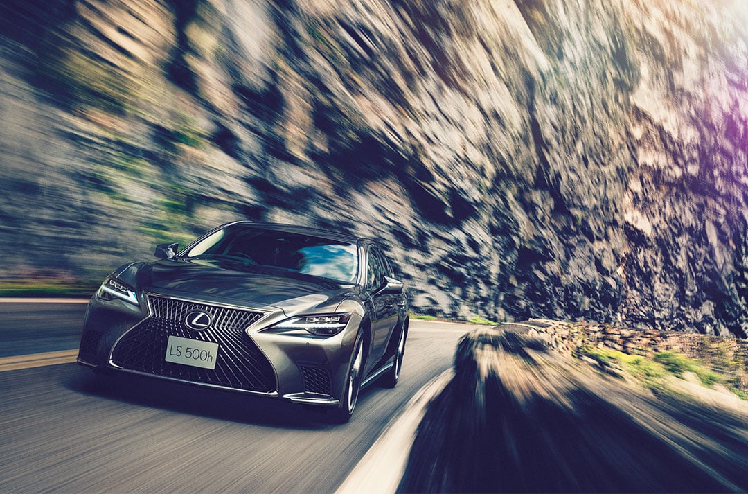 A front-on view of the Lexus LS as it is driven across a road with a rocky background.